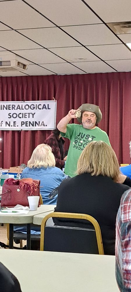 The auctioneer holds up a mineral specimen in front of the MSNEPA banner at the annual auction